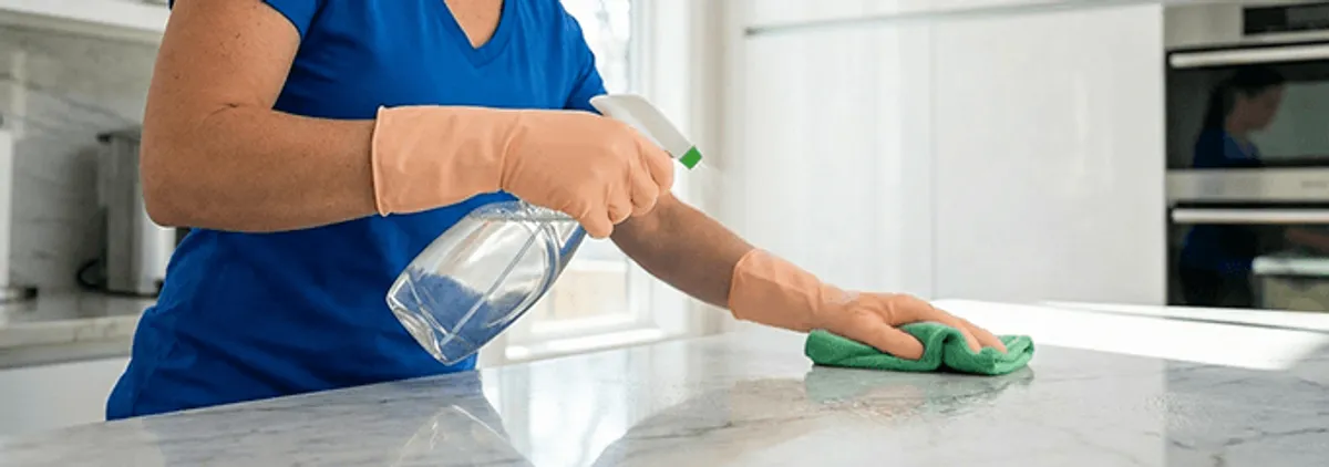 Maid service worker spraying and wiping a kitchen countertop with a microfiber cloth for sanitizing, Gilbert, AZ.